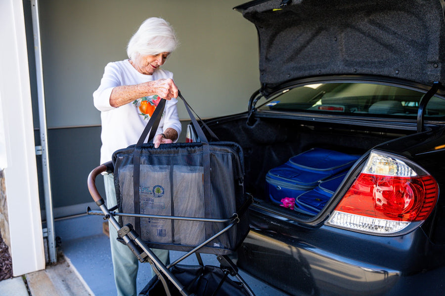 A woman lowers the mesh shopping bag into the frame of her Stability Shopper at the open trunk