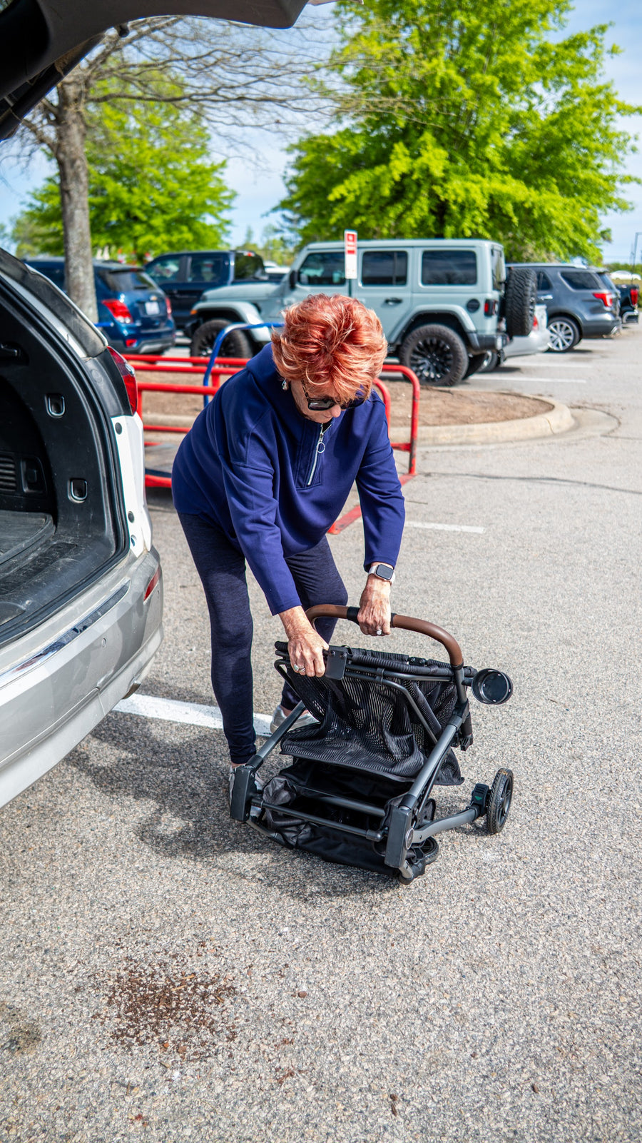 A woman presses the fold button and opens her Stability Shopper beside her car