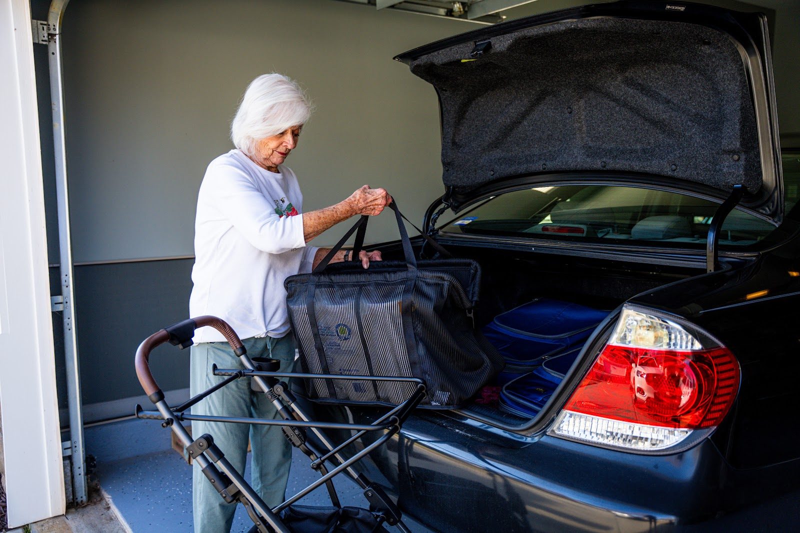 A woman lifts the loaded mesh bag off her Strolee Stability Shopper into the open trunk of her car