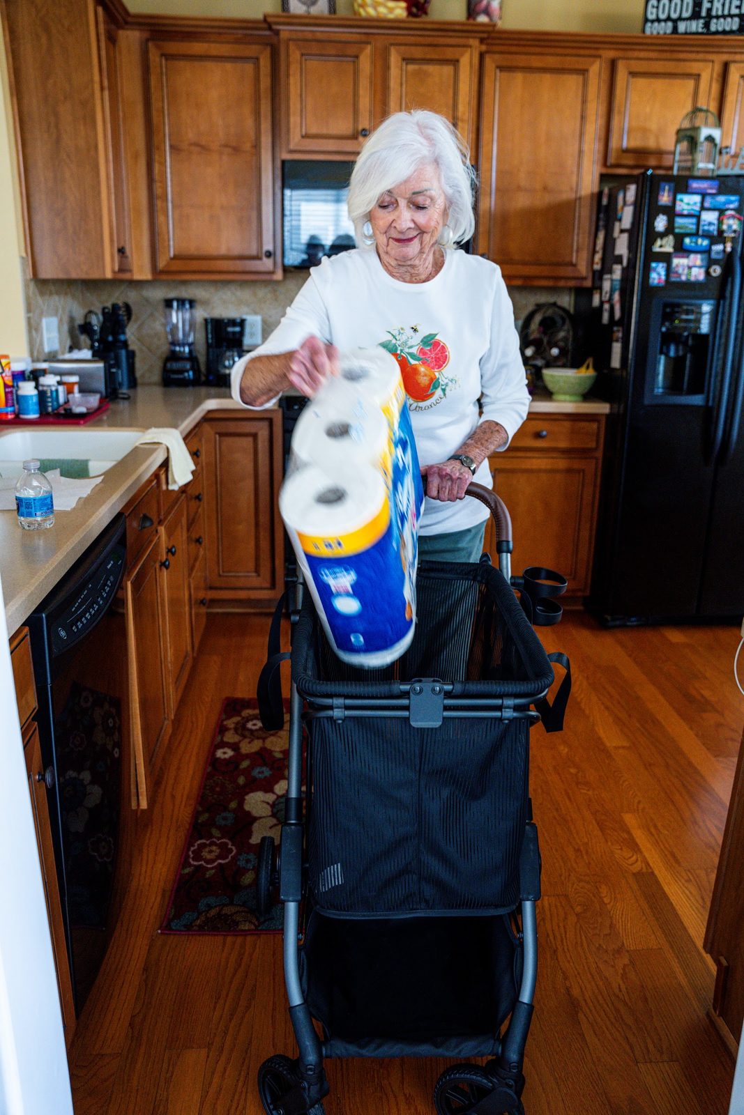 A woman in her kitchen lifts a pack of paper towels into her Strolee Stability Shopper