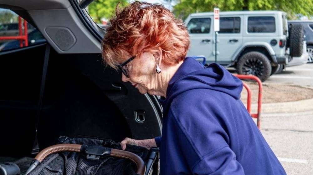 A woman lifts her folded Strolee cart into the trunk of her car