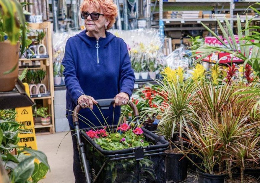 A woman walks a garden center aisle with her Strolee cart, flowers in the bag