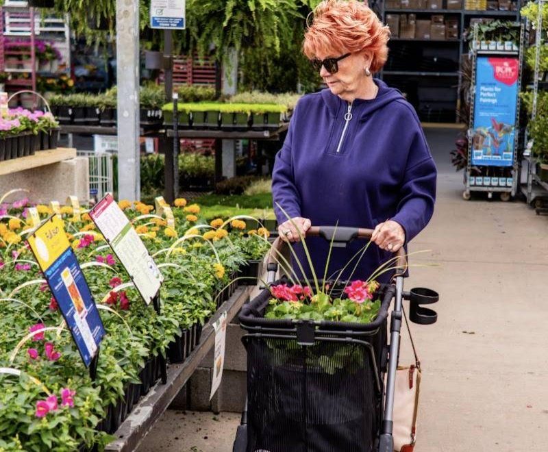 A woman pushes her Strolee cart through a garden center with flowers in the bag