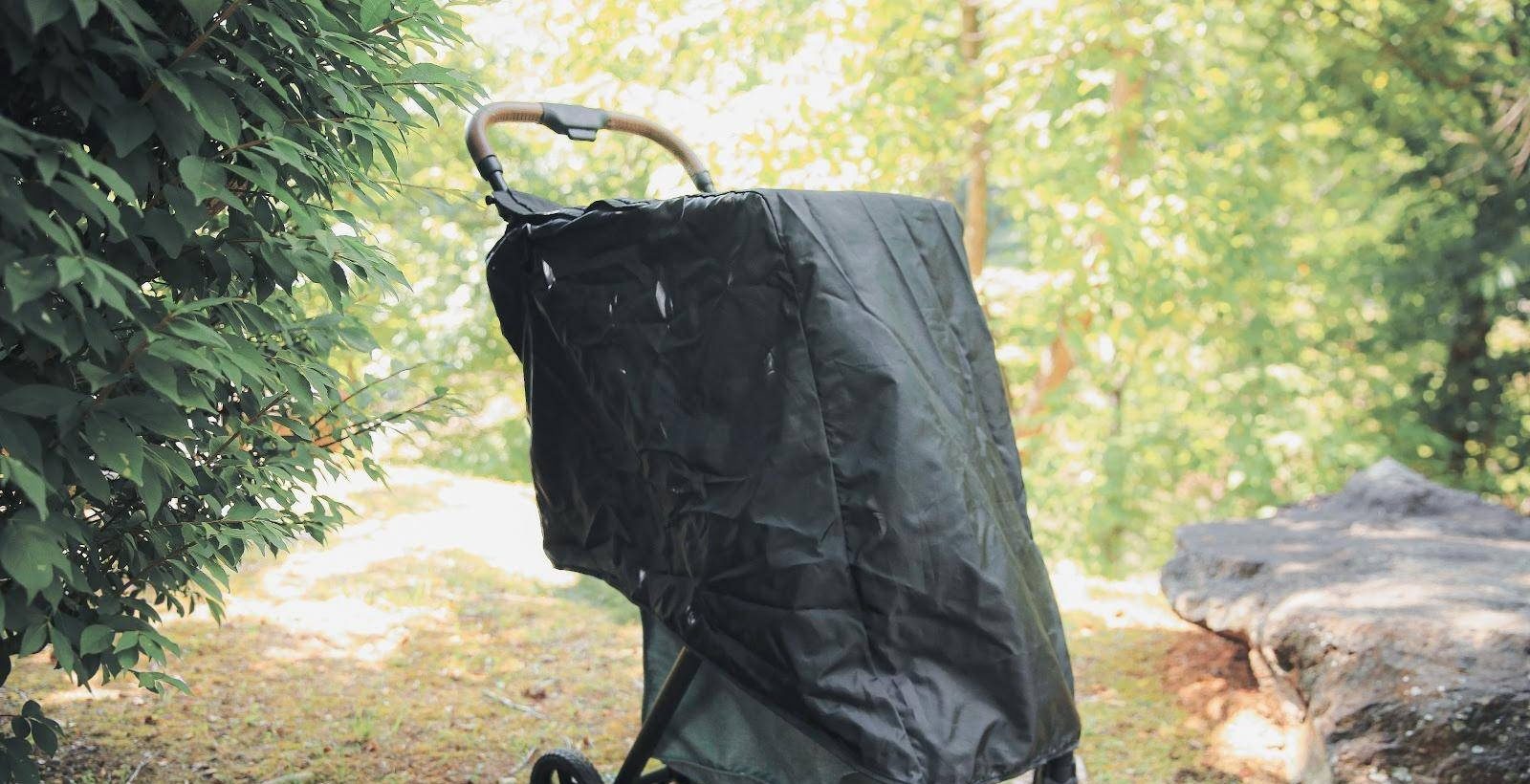 A Strolee cart covered by the rain cover beside a hedge